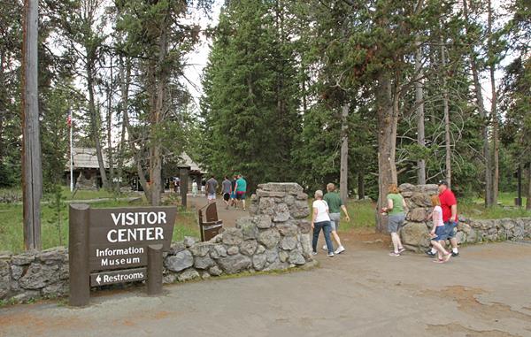 Visitors walk toward a visitor center on a path through pine trees.