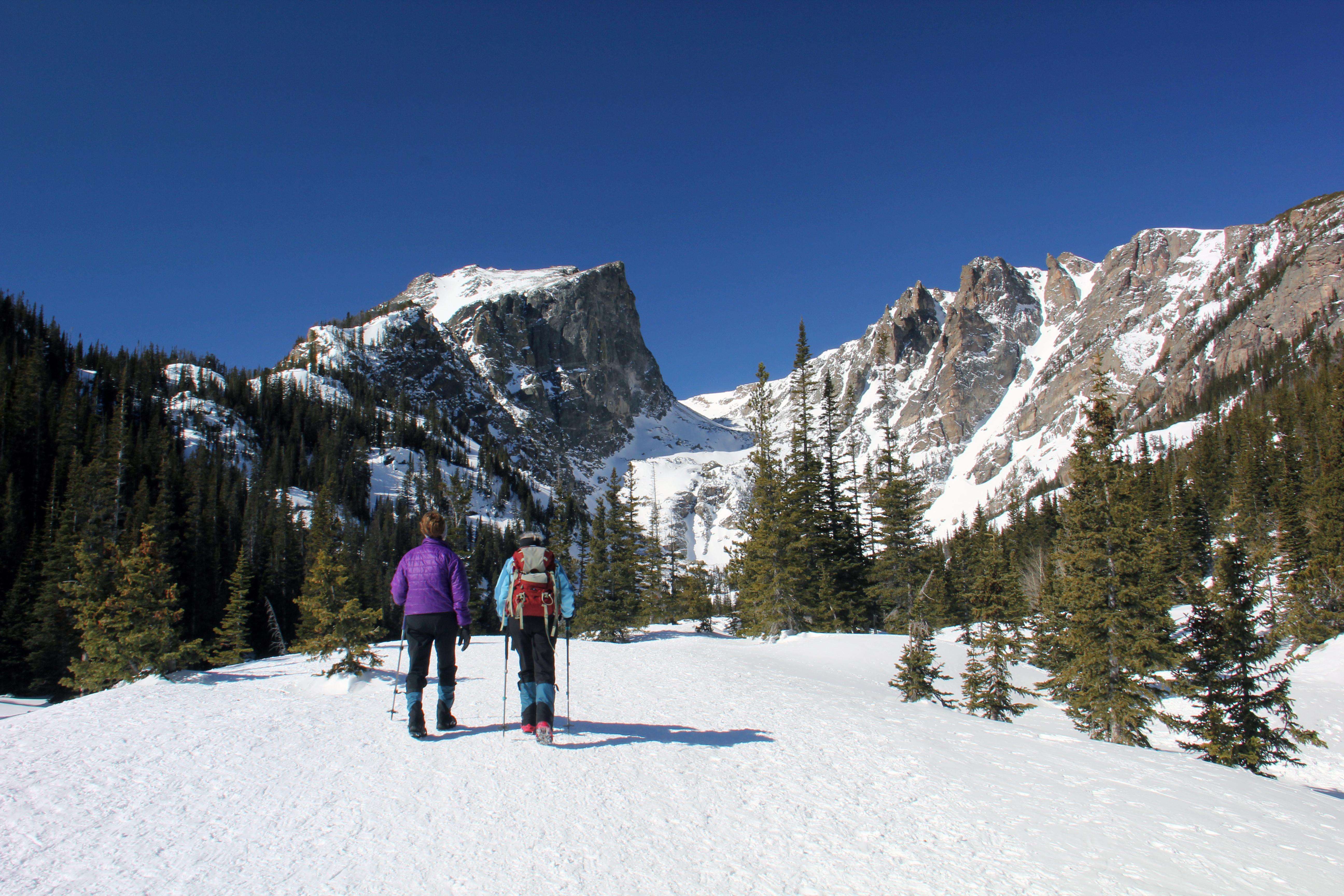 Two people are snowshoeing on a snow-packed trail