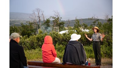 A park ranger in uniform stands in front of a crowd and gestures with their hands.