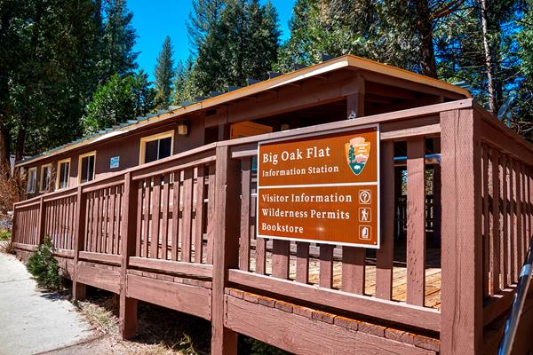 A brown wooden building with a fenced deck has a sign that reads Big Oak Flat Information Station.