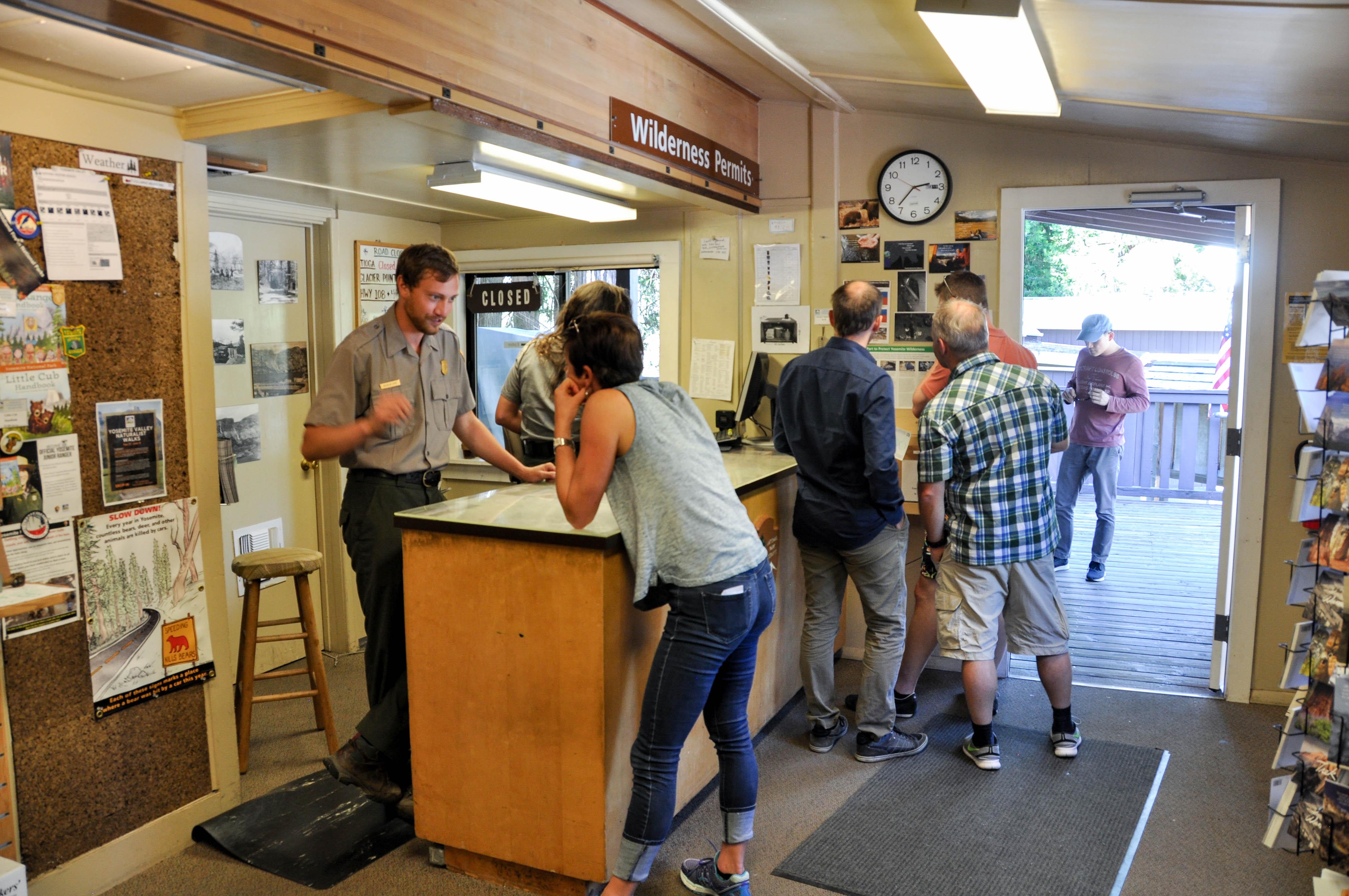 A park ranger stands behind a desk and talks with a person who is hunched over a map on the desk.
