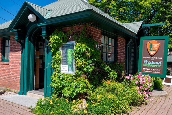 Small brick building with green trim and a hanging sign with the NPS arrowhead
