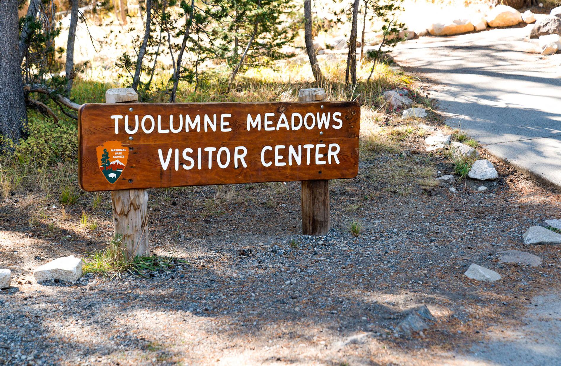 A brown wooden sign reads Tuolumne Meadows Visitor Center and has a National Park Service logo.