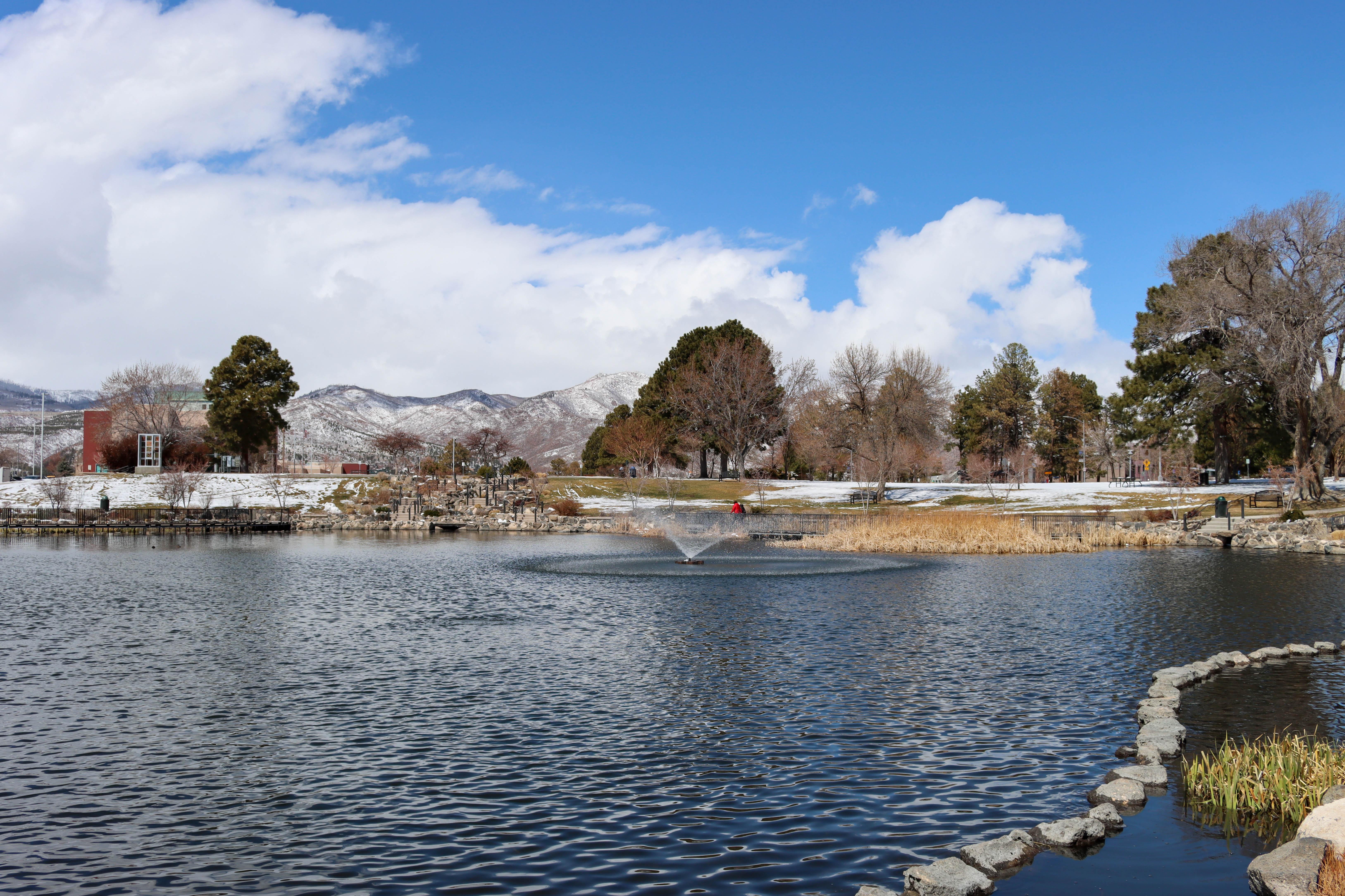 a landscaped pond with fountain in front of snowy mountains and a blue sky with clouds