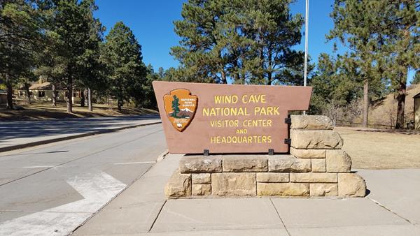 a brown wood and stone sign reading "wind cave national park visitor center and headquarters"