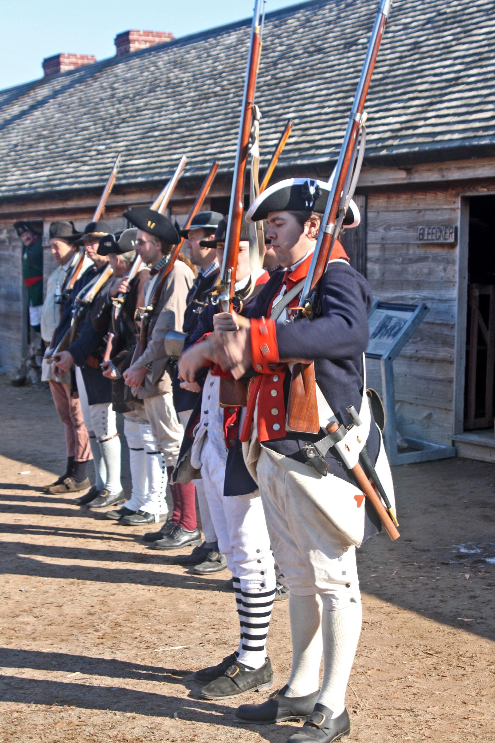 Soldiers stand in a neat row holding their muskets.