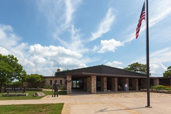 A stone visitor center building with an American flag and a sign out front.