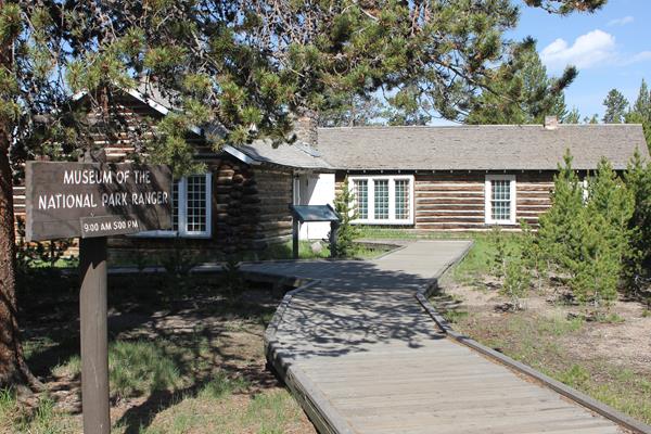 A wooden boardwalk leads past pine trees to the Museum of the National Park Ranger