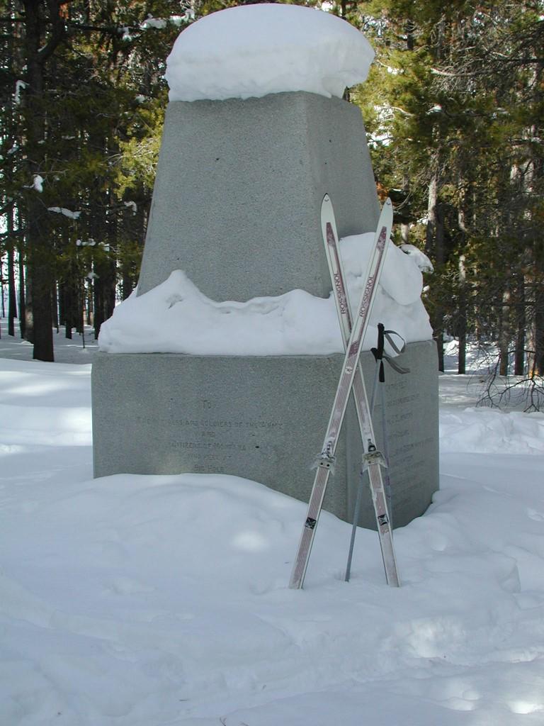 cross country skis rest against a large granite monument on a snowy day.
