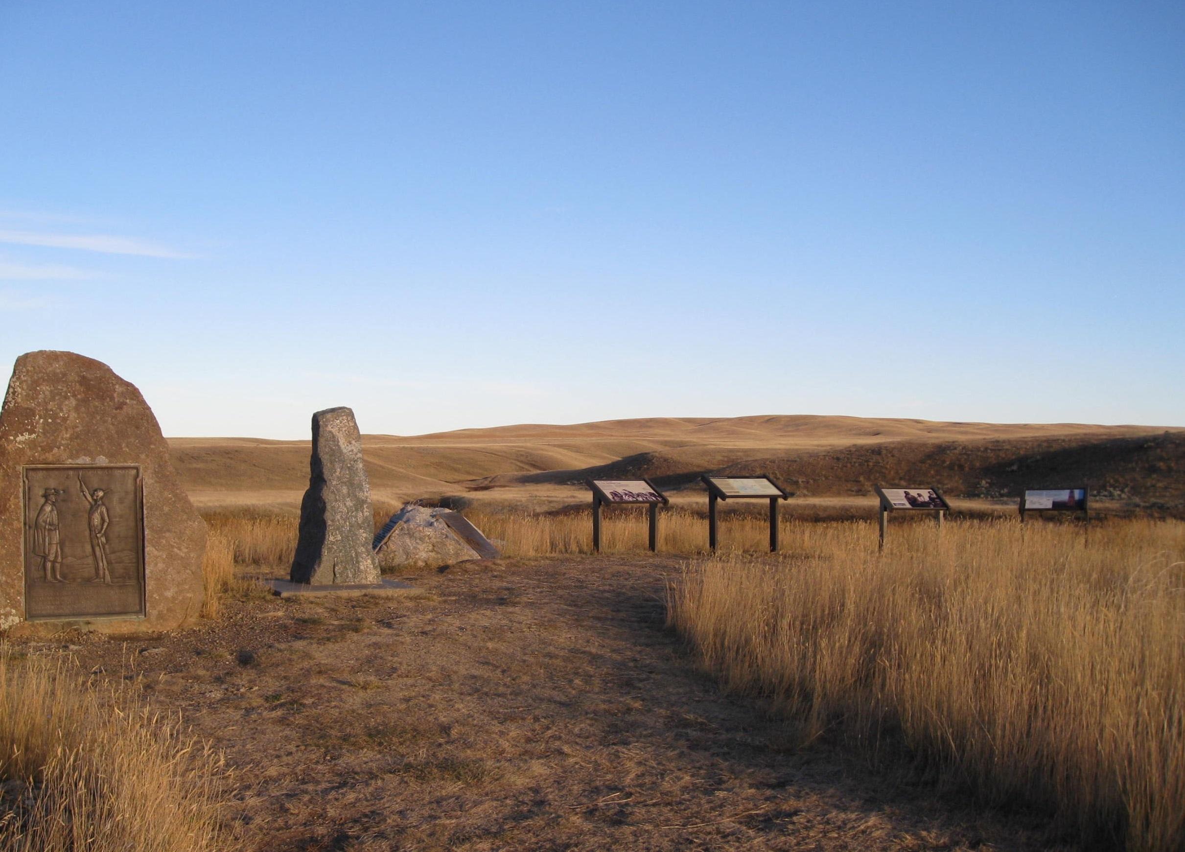 Three large stone monuments and four interpretive signs overlook a series of low hills.
