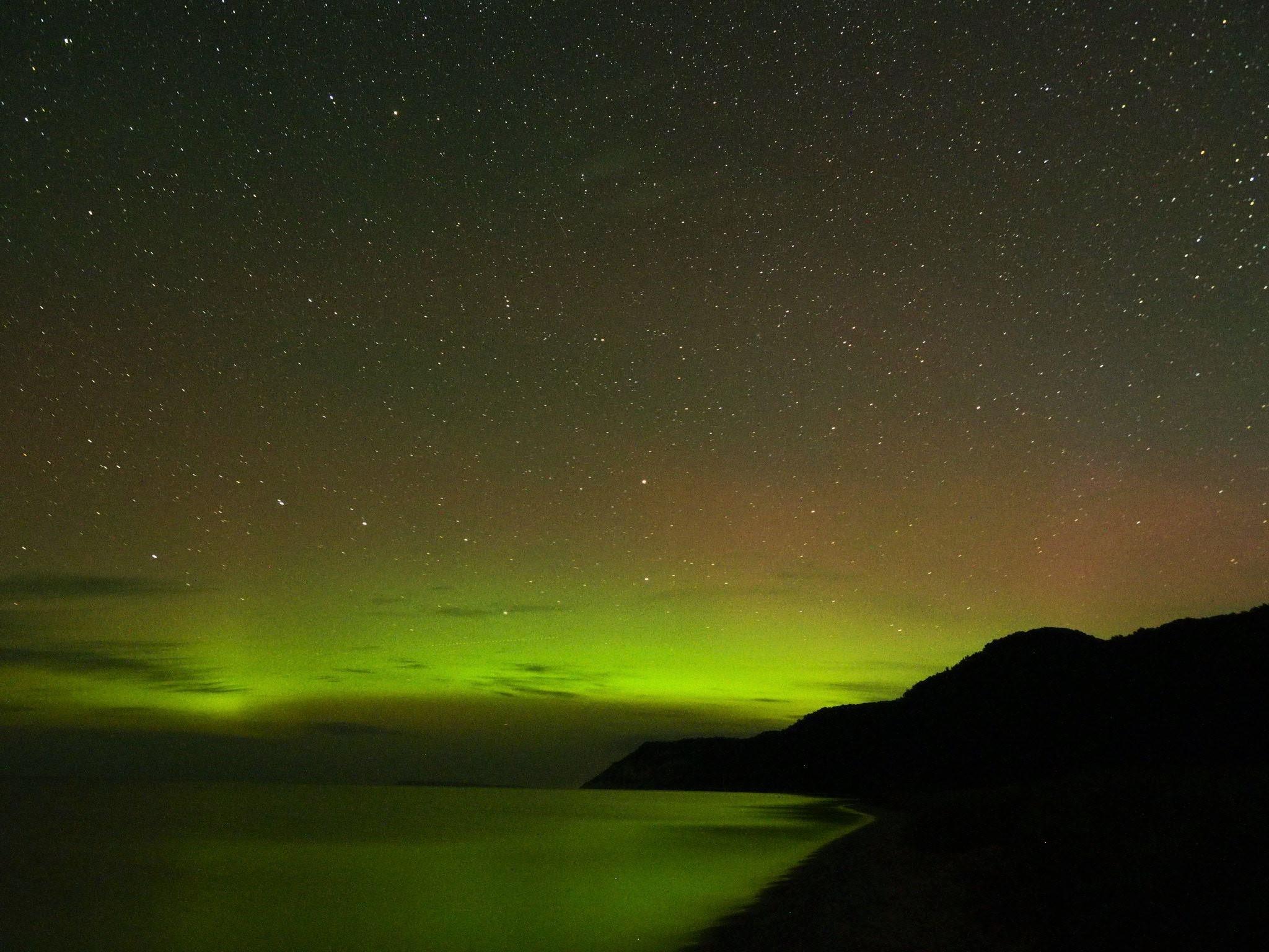 A glowing yellow and red northern light display with stars over a body of water