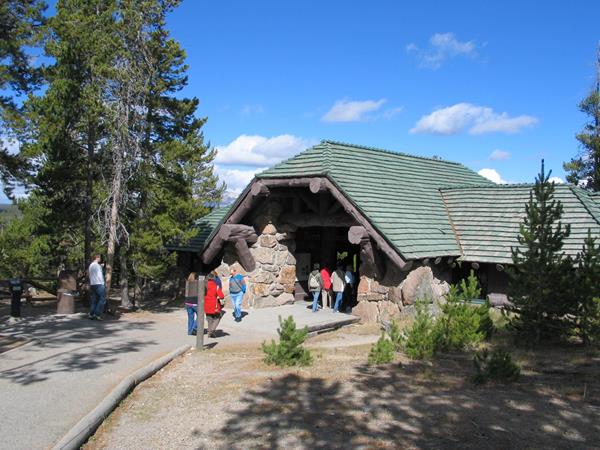 Visitors stand in front of a log and stone structure.