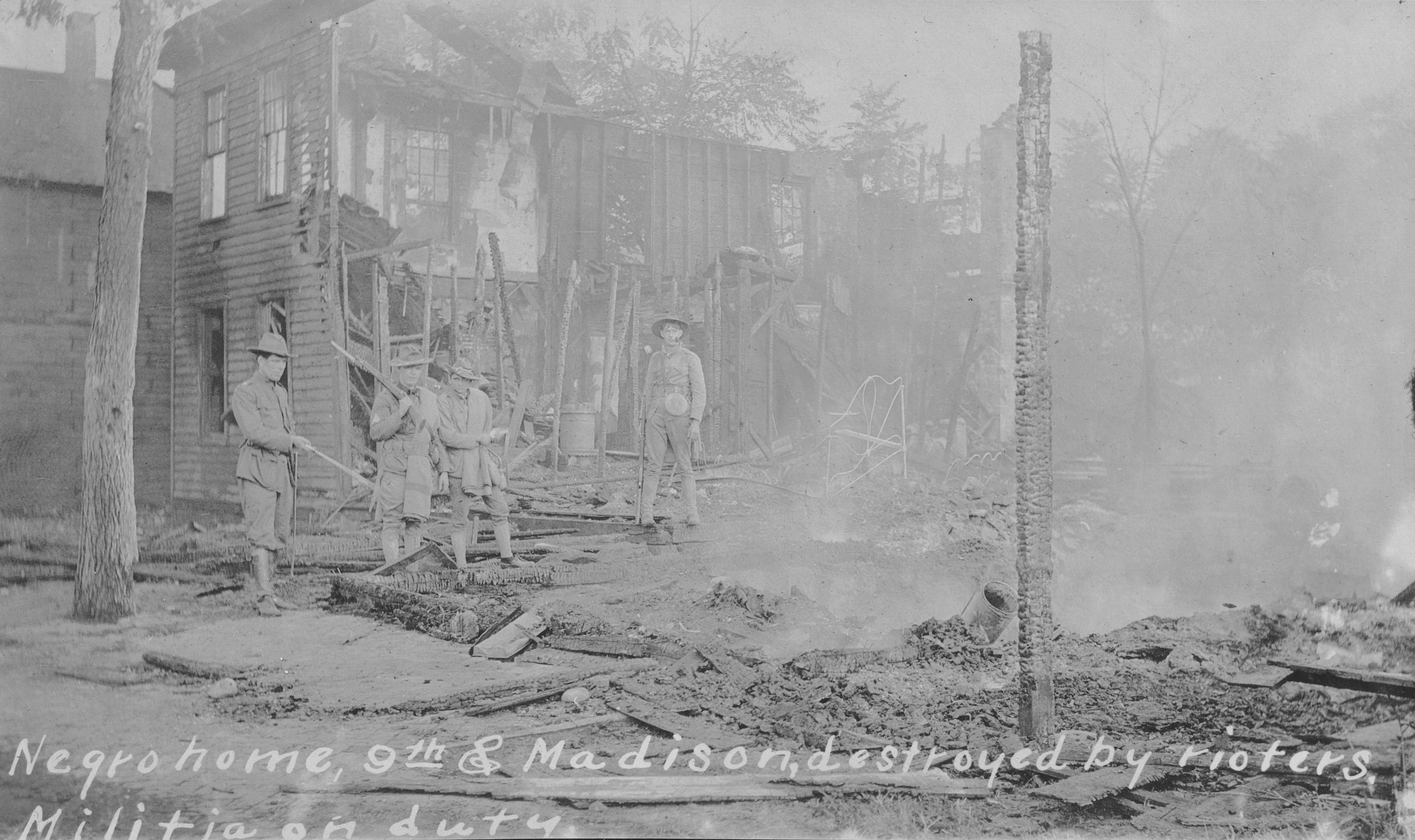 Historic photo of militia members standing in the remains of a burned building.