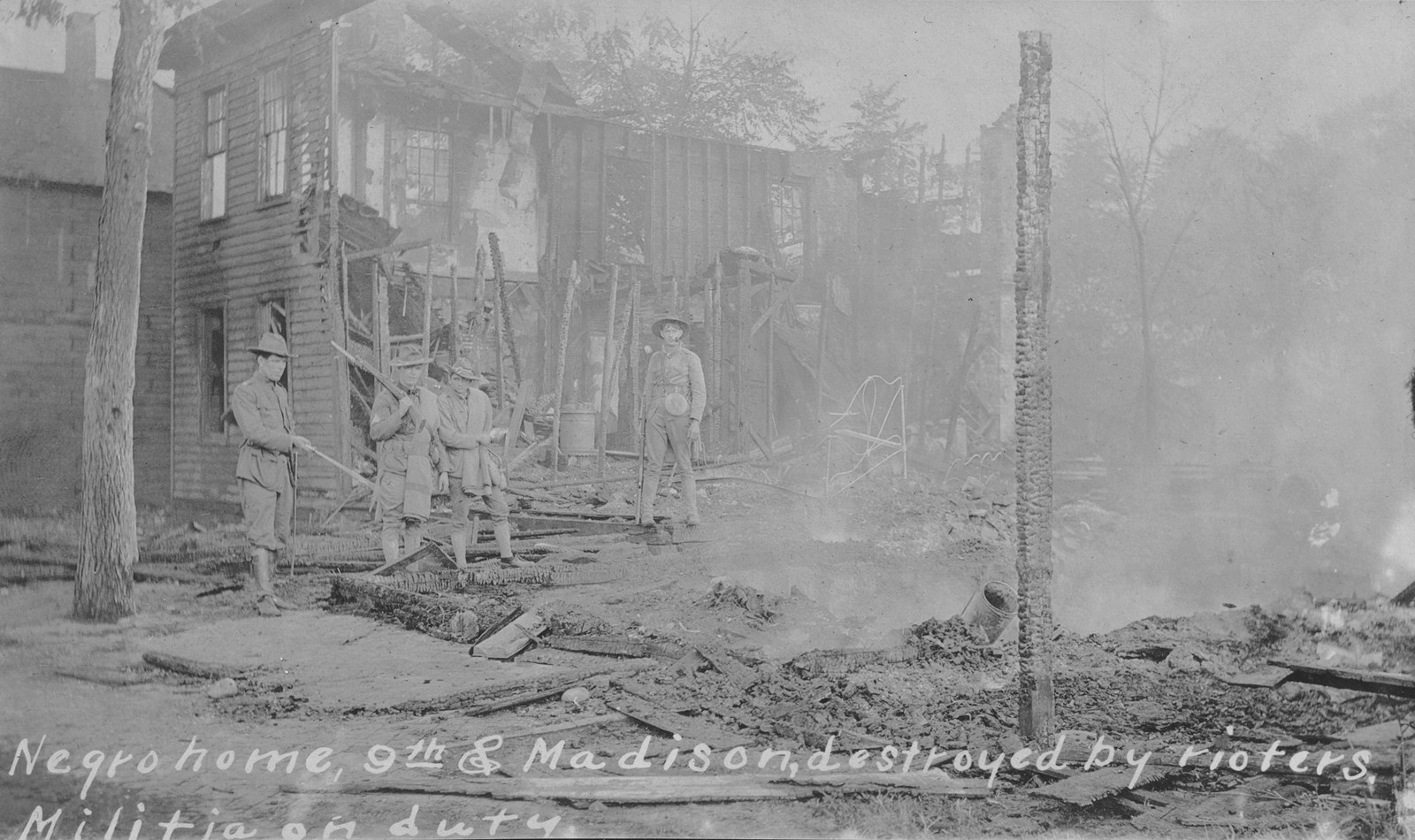 Historic photo of militia members standing in the remains of a burned building.