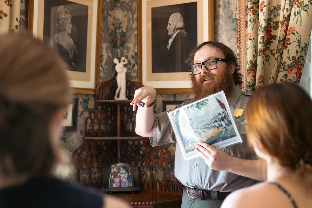 Park ranger holding historic illustration in front of prints of Martha and George Washington