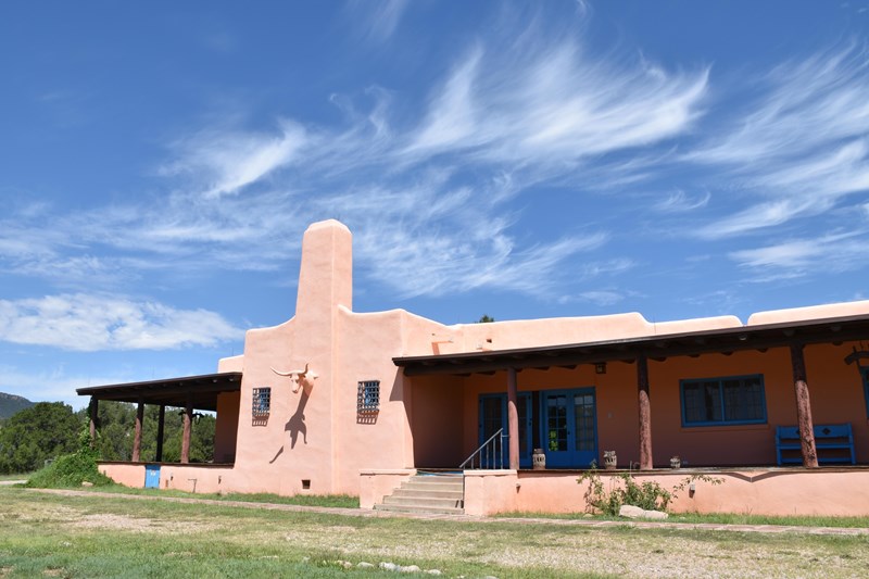 Forked Lightning Ranch House Pink-tan building with chimney and long covered porches at sides, steer head decoration center.