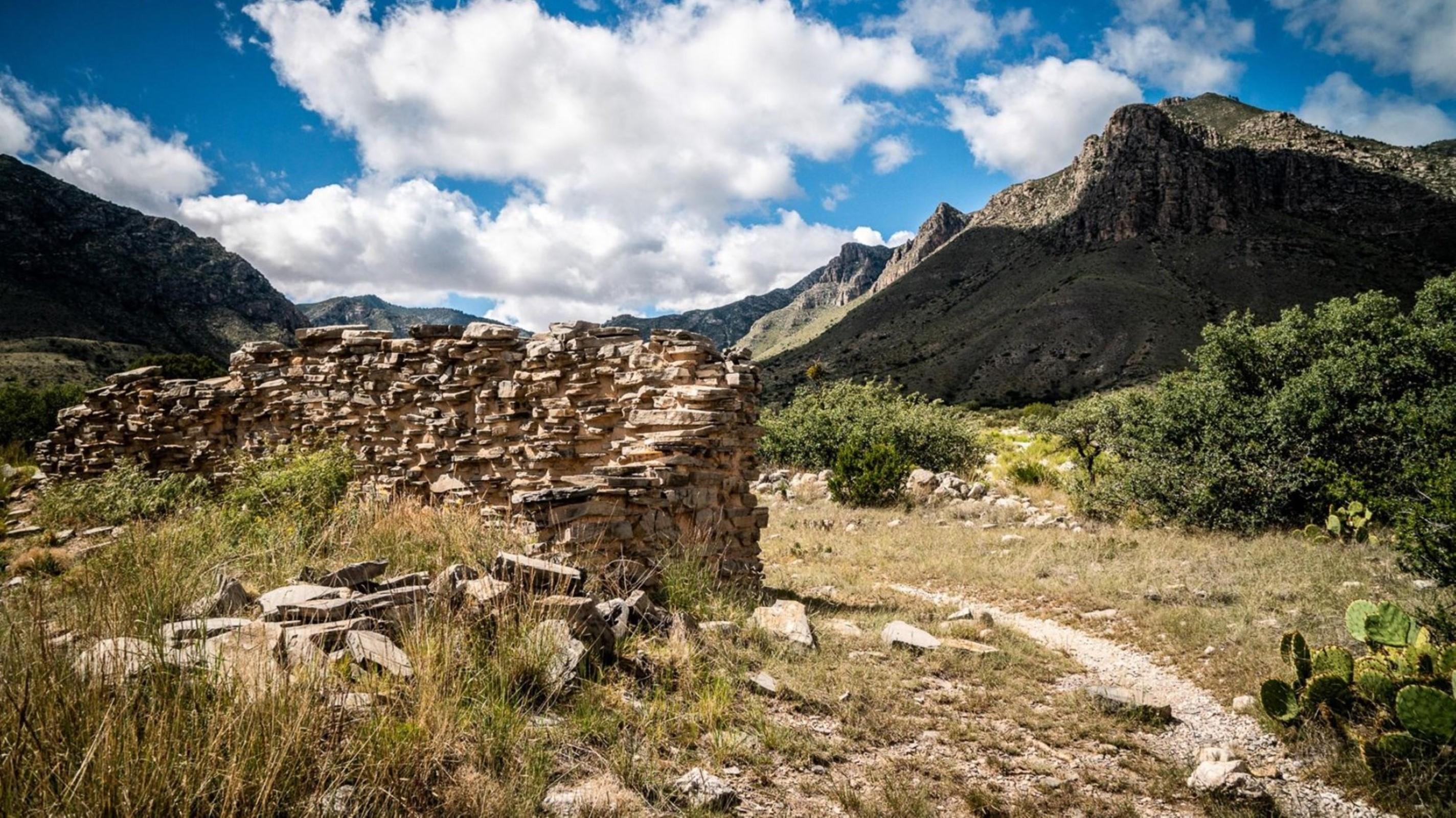 A historic stone wall stands in ruins next to a hiking trail leading into the Guadalupe Mountains NP