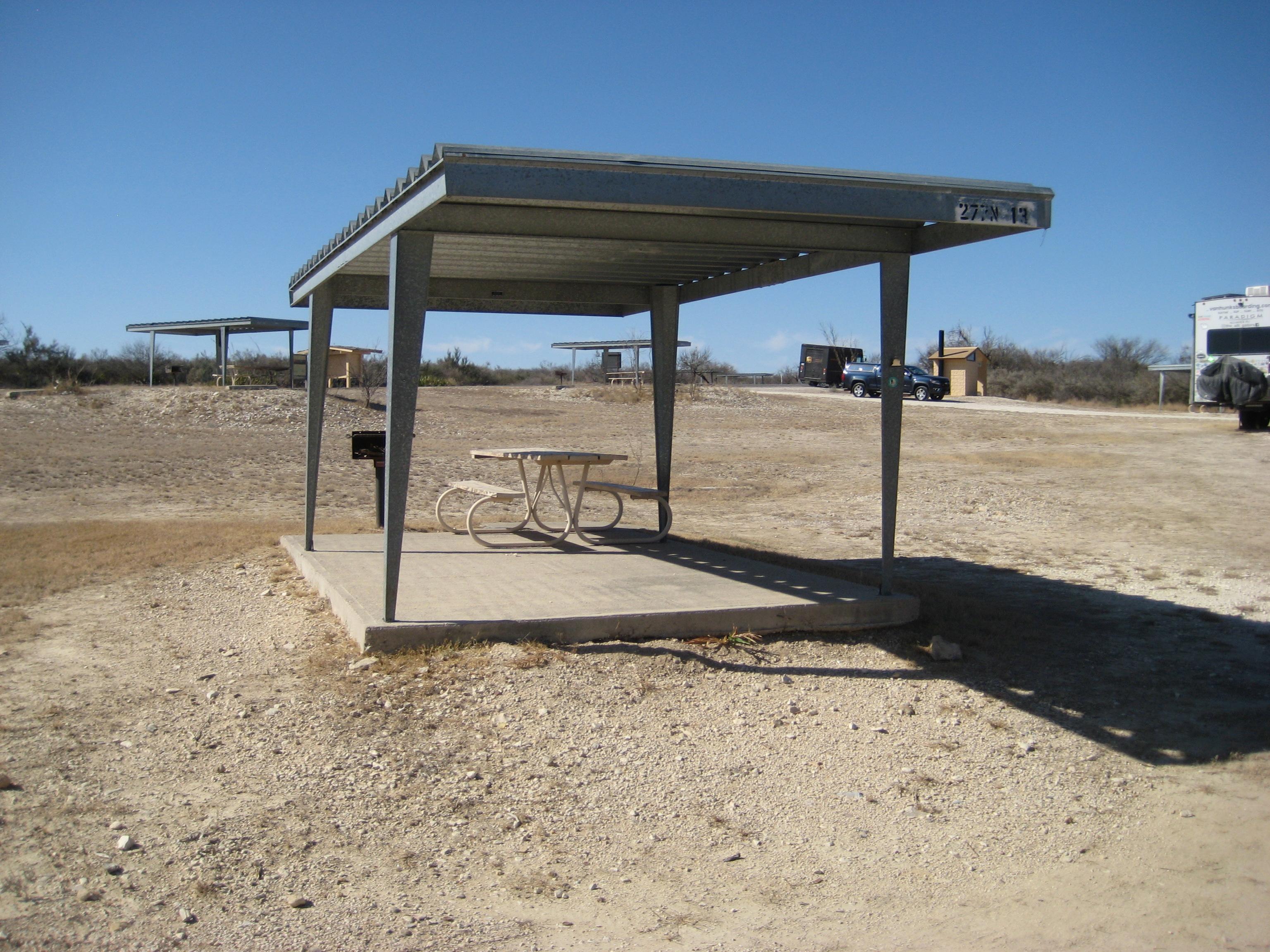 Picnic table on cement pad under shade shelter with BBQ grill