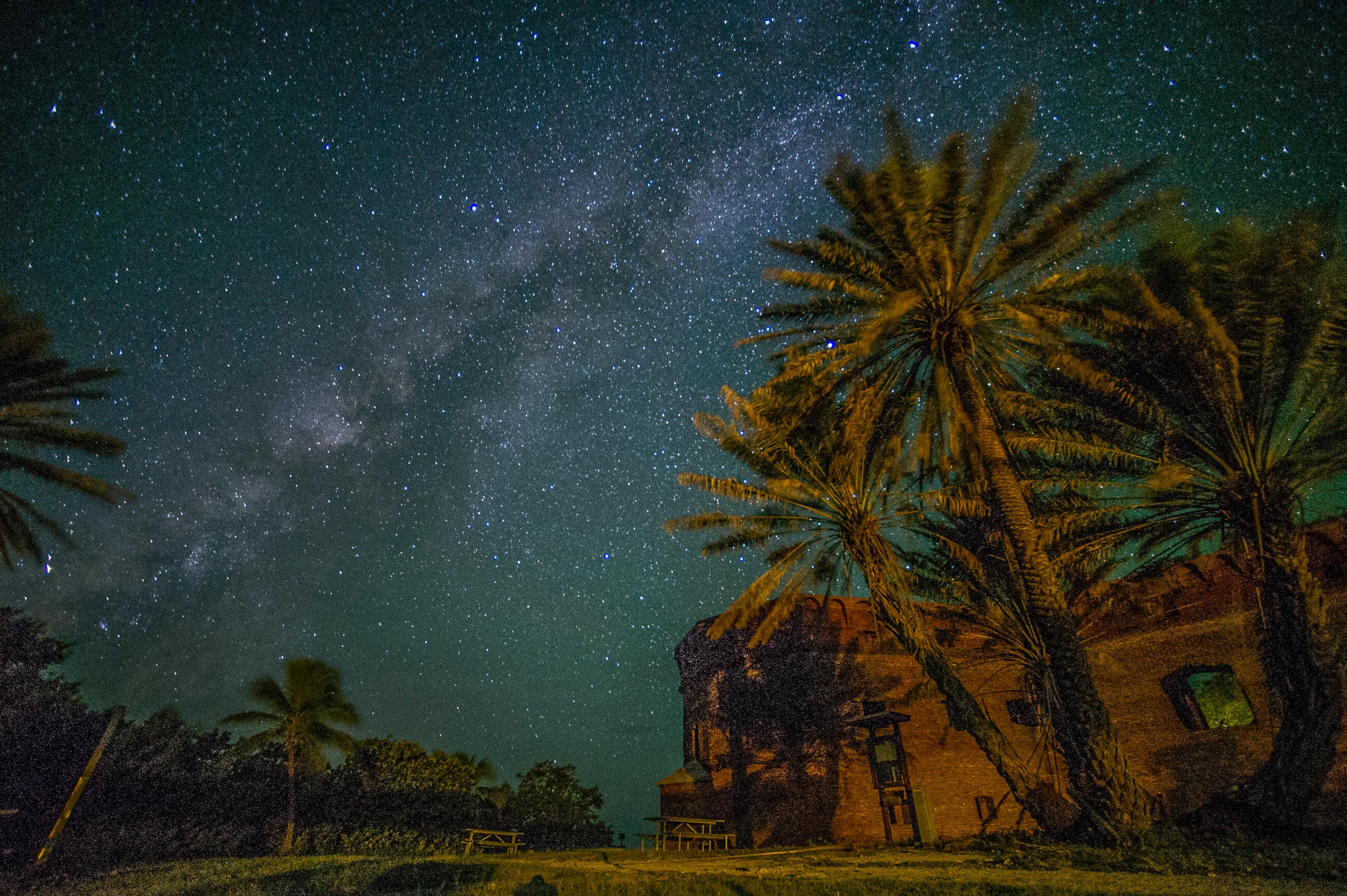 A clear view of the Milky Way as it stretches over a campground and fort.