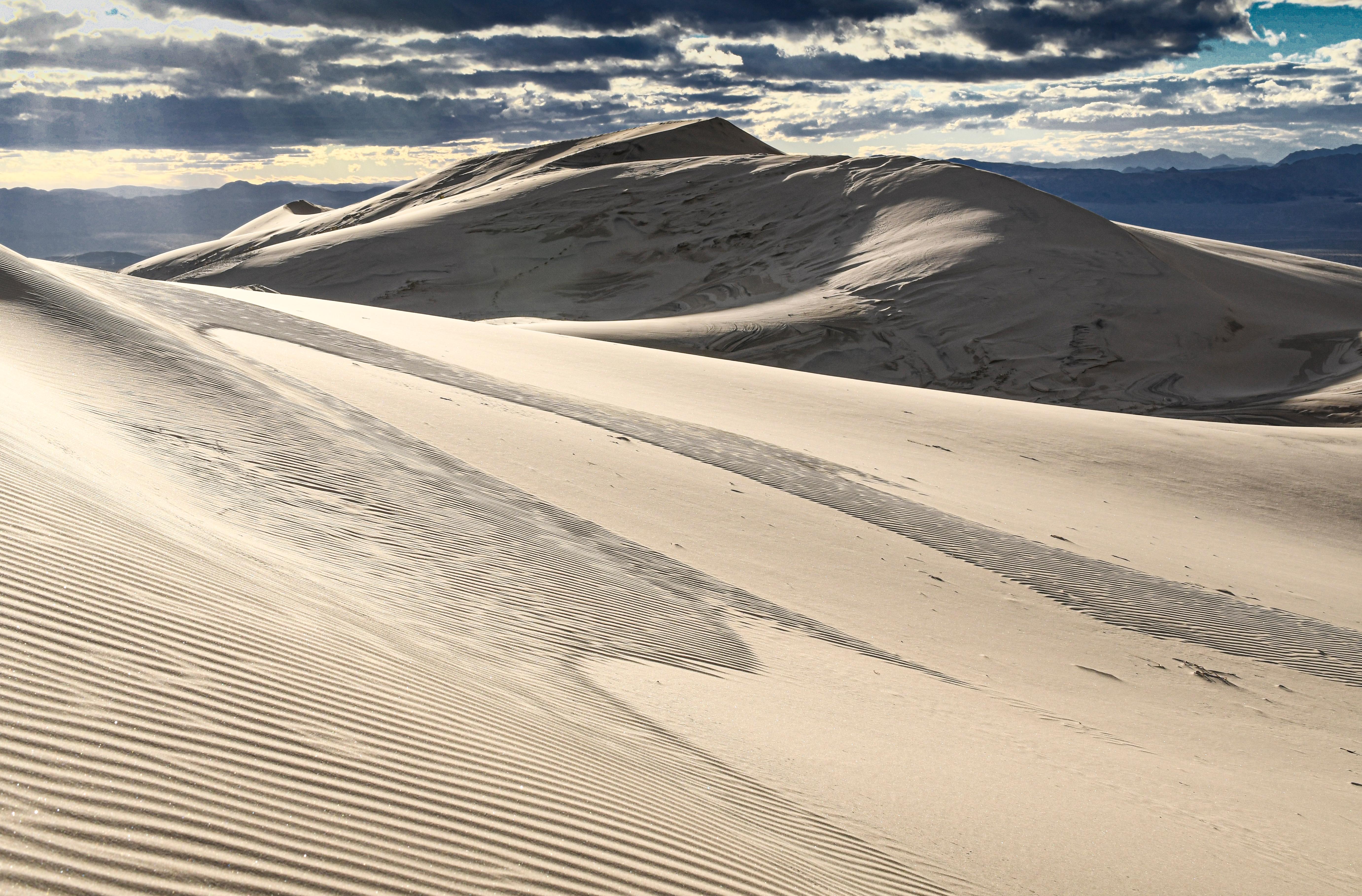 Kelso Dunes with rays of light coming through the clouds. Mountains in the background..