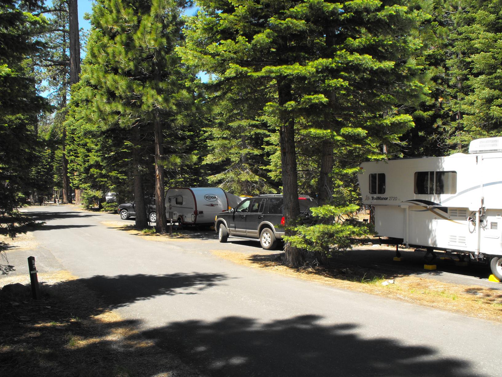 A paved road lined by campsites containing trailers and vehicles.