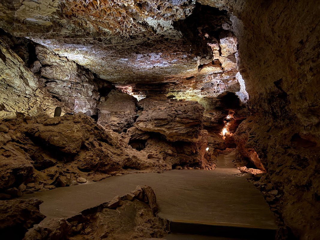 View of a cave room with yellowish-brown rocks and a criss-cross pattern of boxwork on the ceiling.