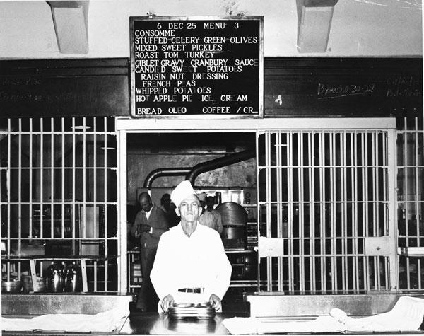 Cook serving Christmas dinner with menu posted above.