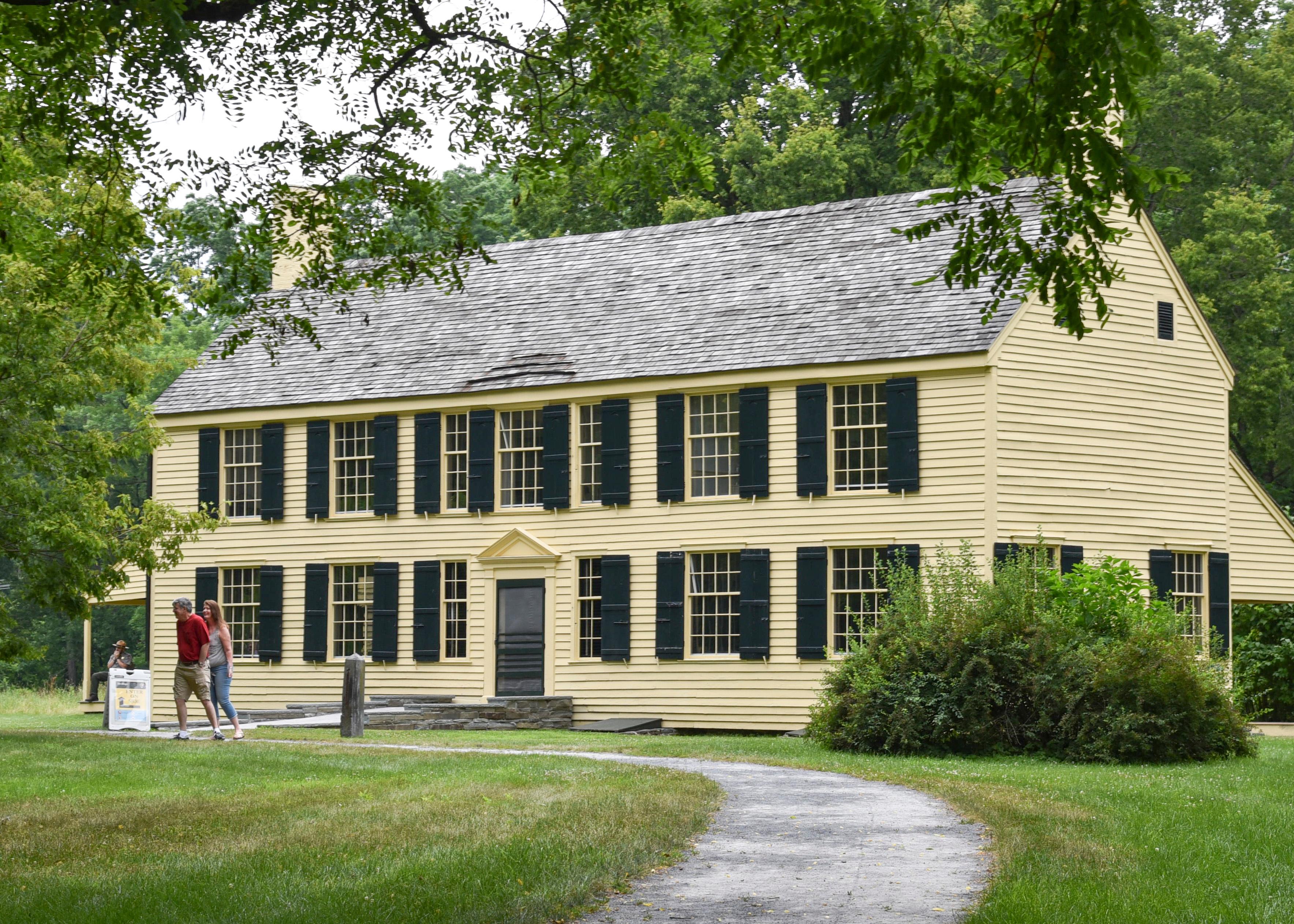 A narrow, winding path leads through some trees to a 2-story yellow house.