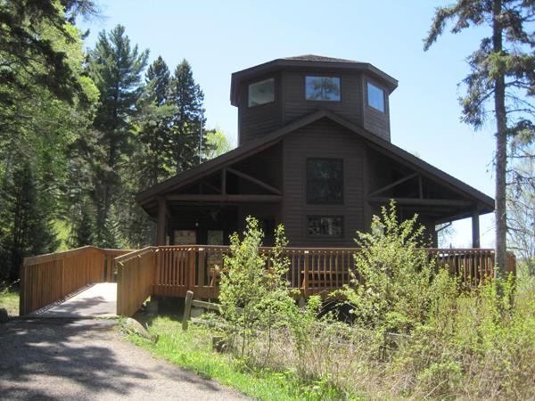 A brown building with a ramp leading to it is surrounded by green vegetation.