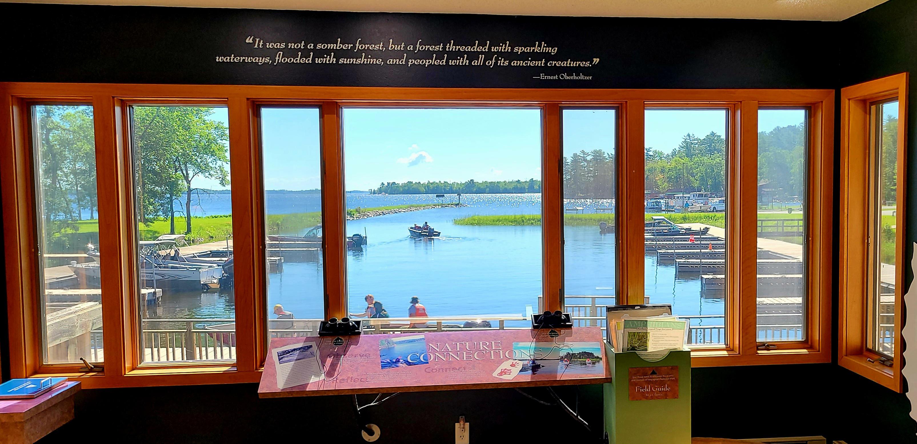 Photograph looking out of windows towards blue lake with interpretive exhibits in the foreground.