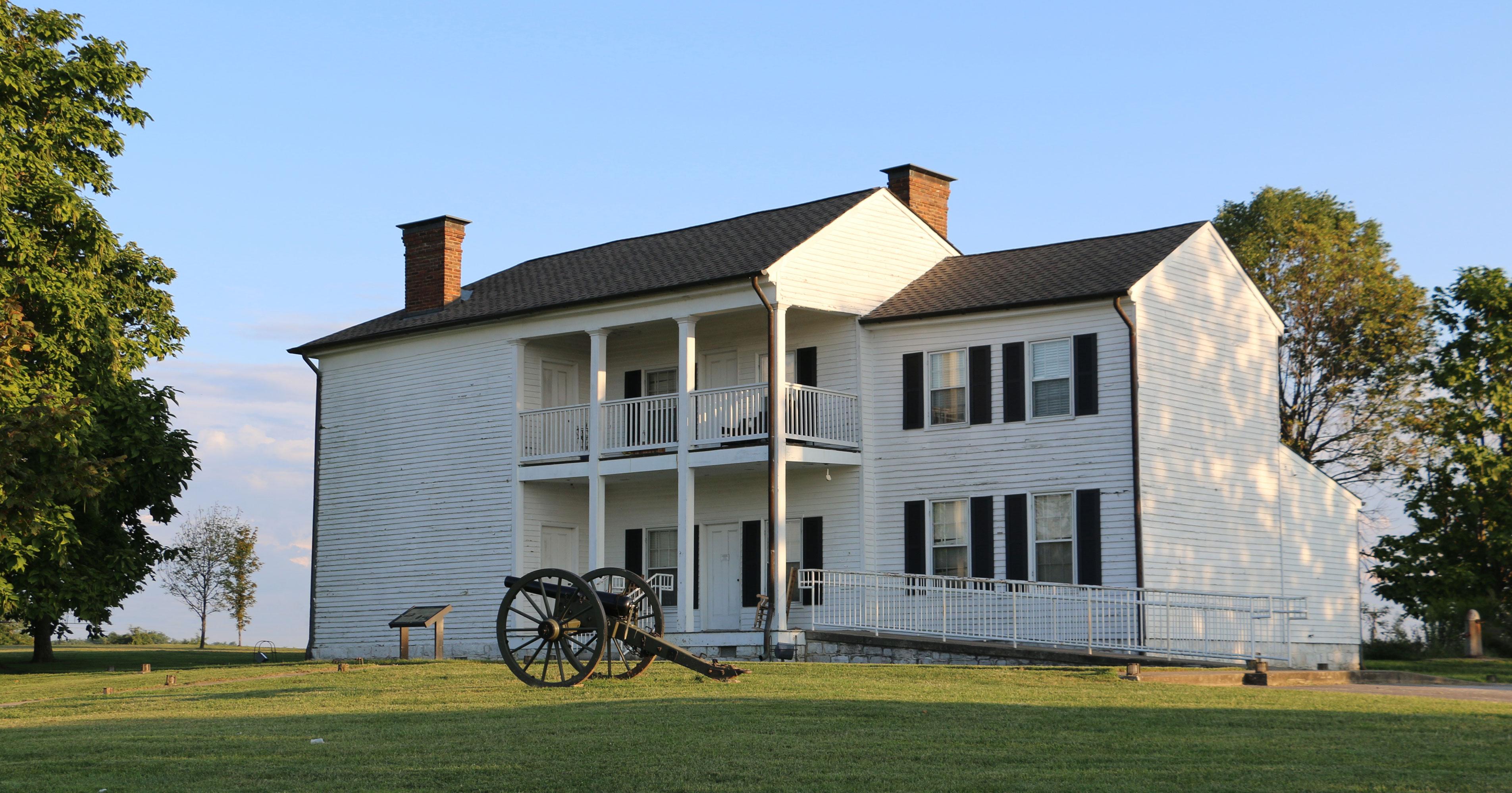 A white, 2 story farm house with a Civil War cannon sitting in front of it