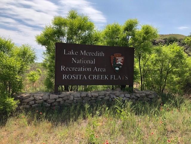 A National Park Service brown sign with Rosita Flats written on it beside cottonwood trees.