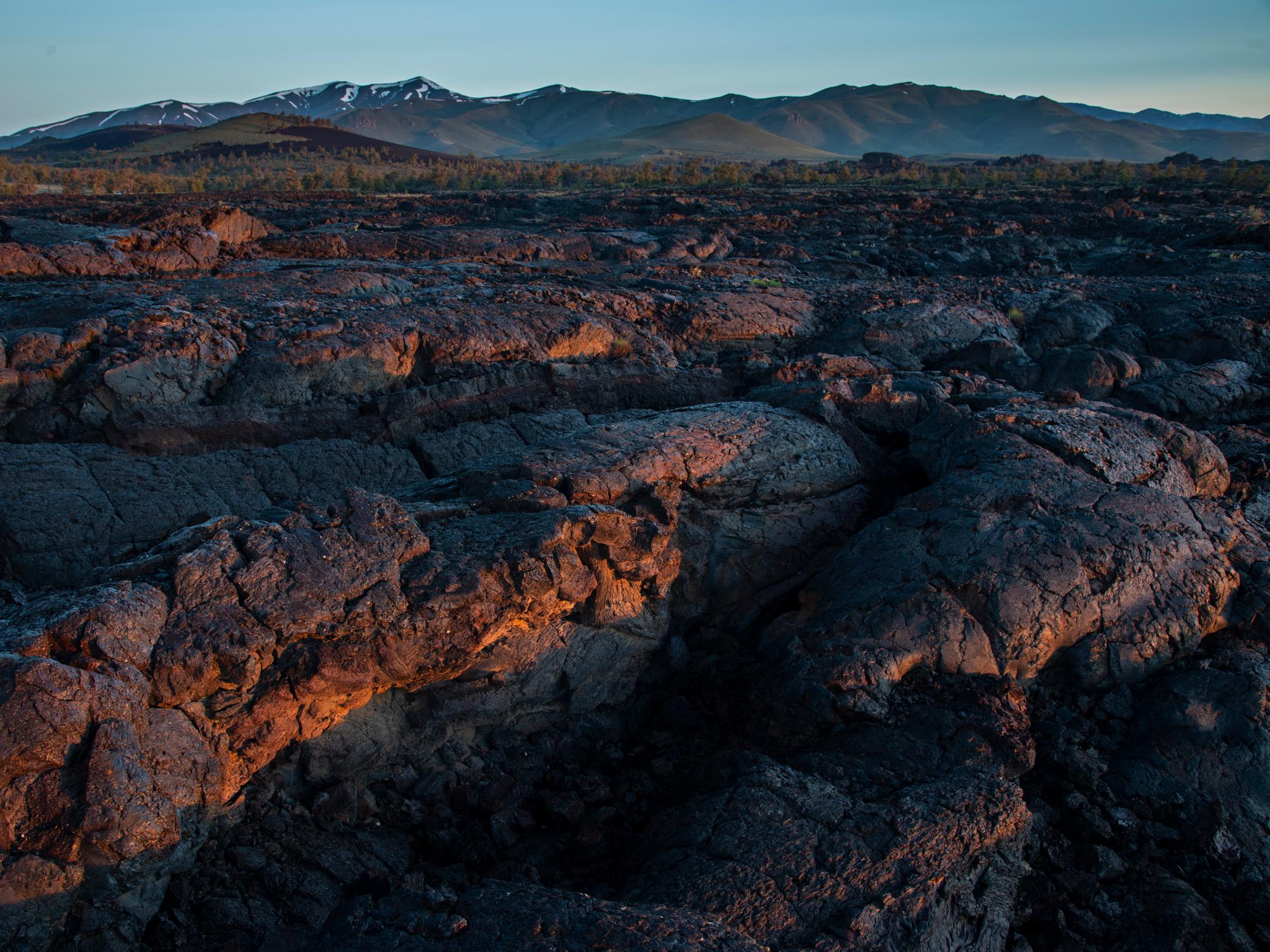 A close-up shot of a folded, waving sea of lava rock, with mountains in the far distance.