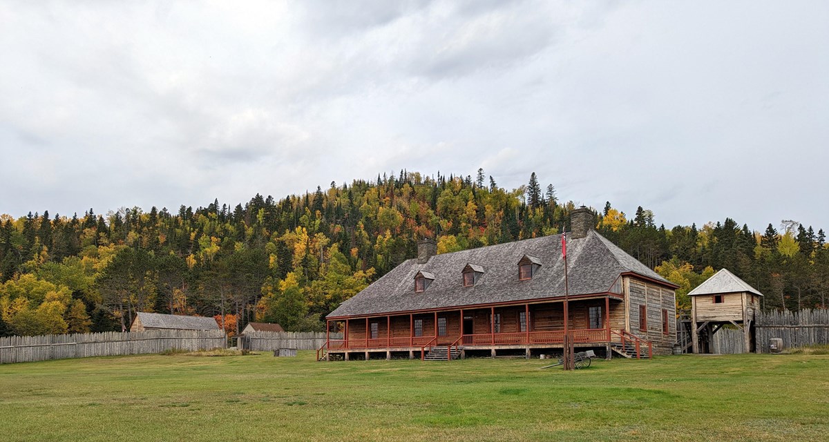Historic buildings with a lawn in the foreground and hill in fall colors behind.