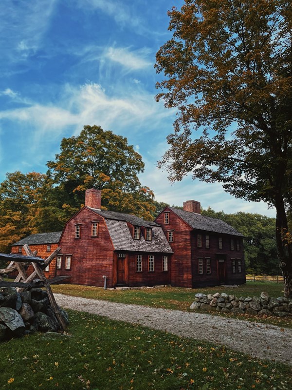 A wooden colonial era house surrounded by tall trees