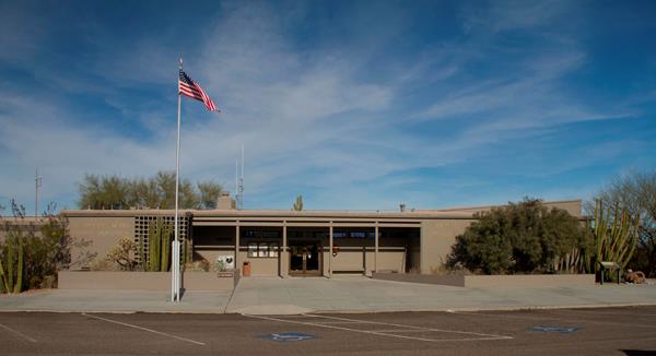A grayish, brown one story building with planters surrounding the front and an American flag outside