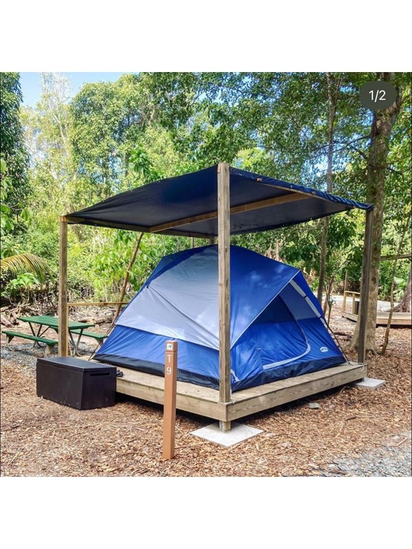 A blue and grey tent pitched on a wood platform with a blue tarp with woods in the background