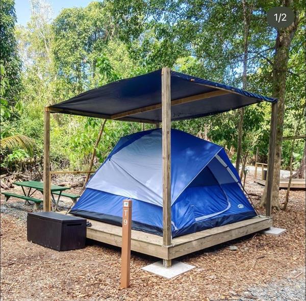 A blue and grey tent pitched on a wood platform with a blue tarp with woods in the background