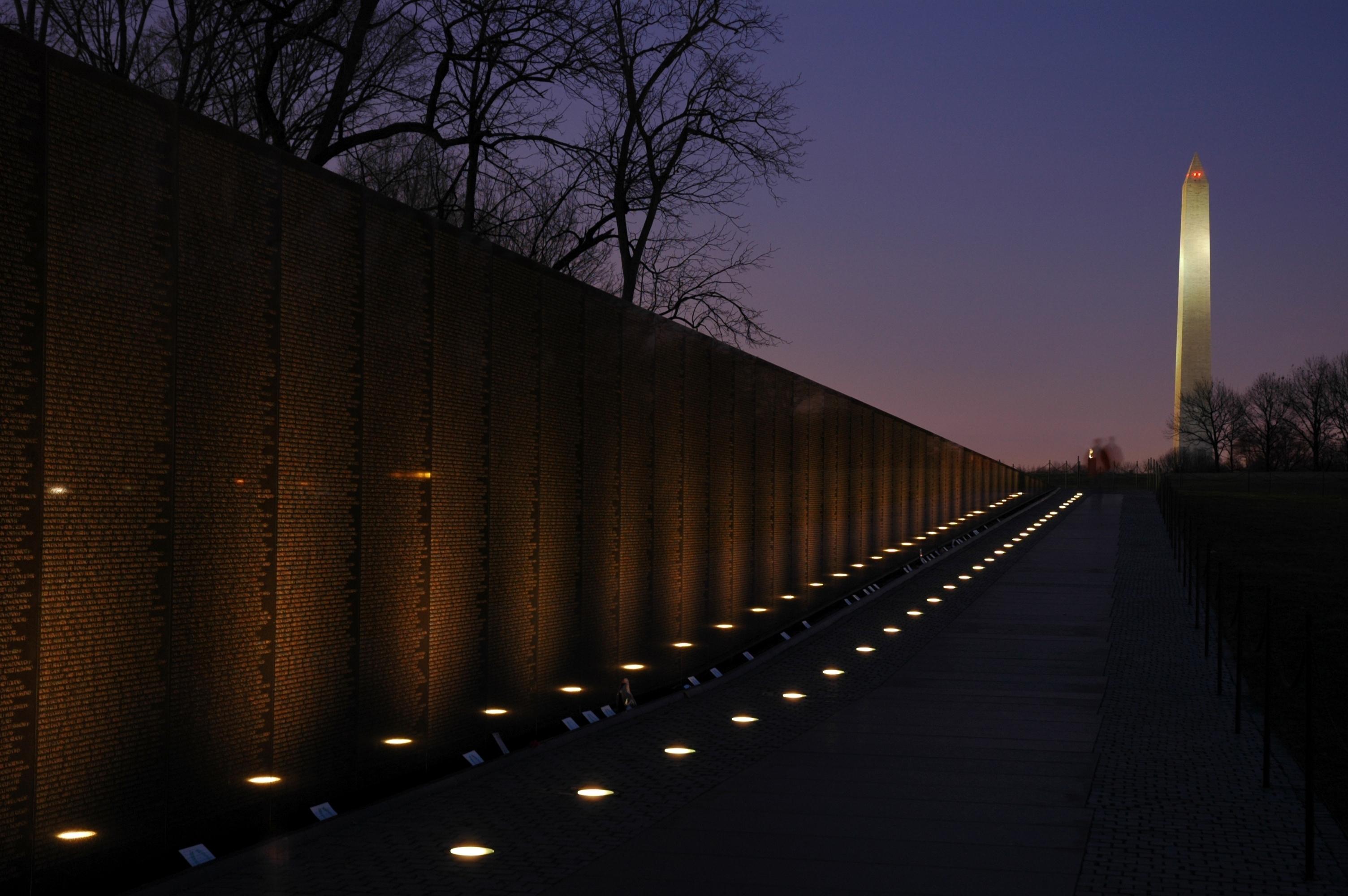 Lights glow at the base of the wall of the Vietnam Veterans Memorial with Washington Monument.
