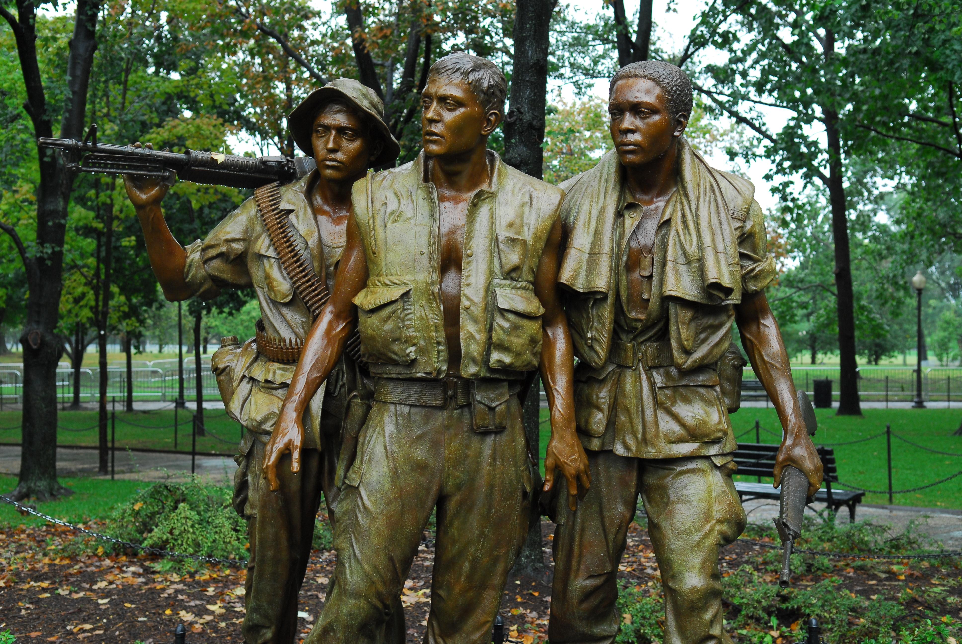 A bronze statue of three soldiers standing together, carrying weapons, and looking to their right.