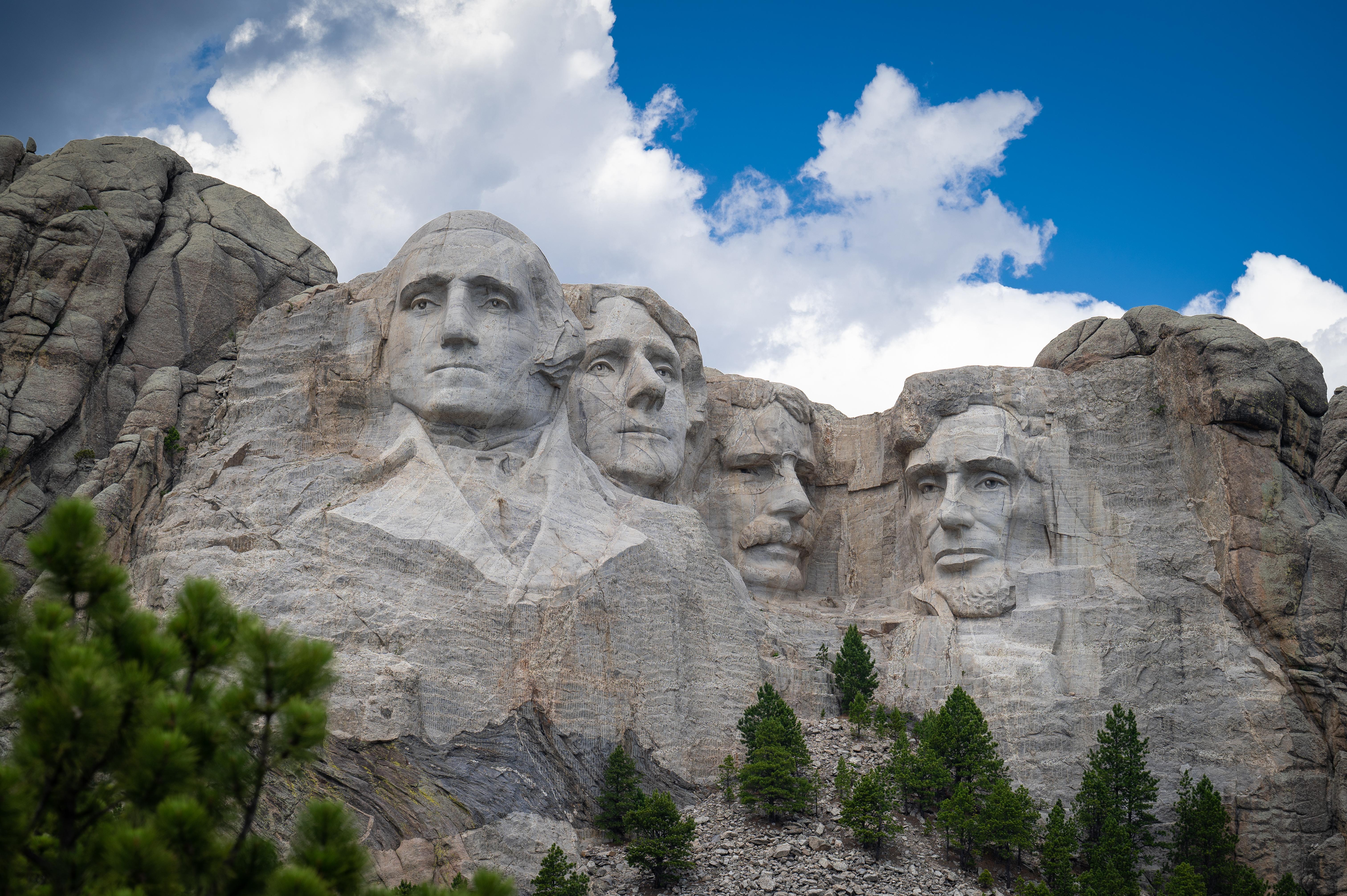 Photo of Mount Rushmore under a bright blue sky with puffy clouds floating over.