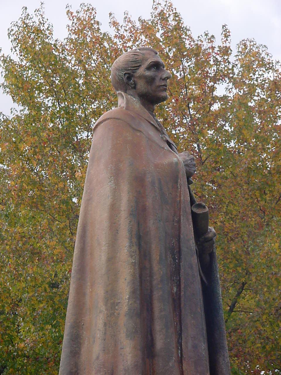 Statue of a man wearing a cloak with trees in background