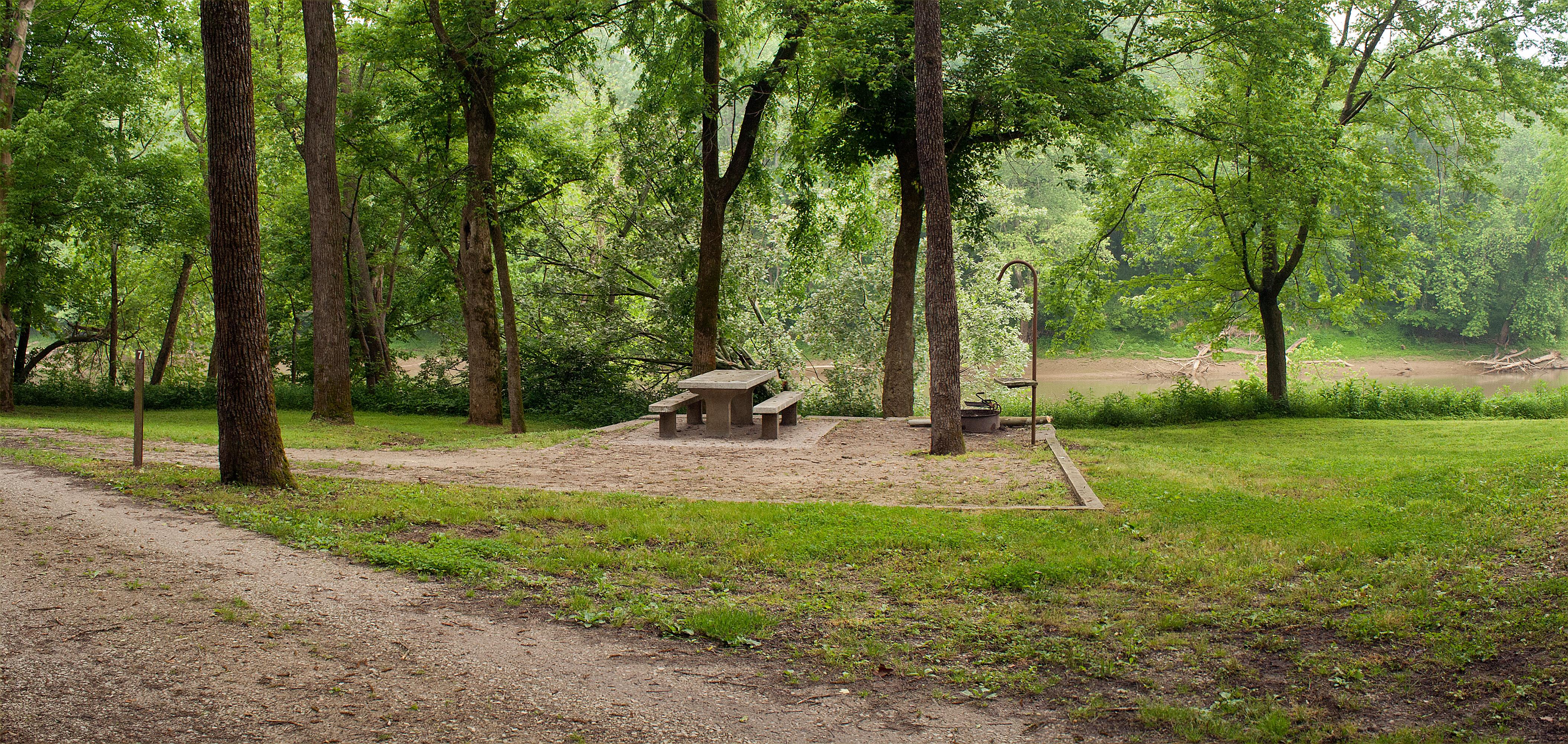 An unoccupied campsite with concrete picnic table, fire ring and lantern hook.