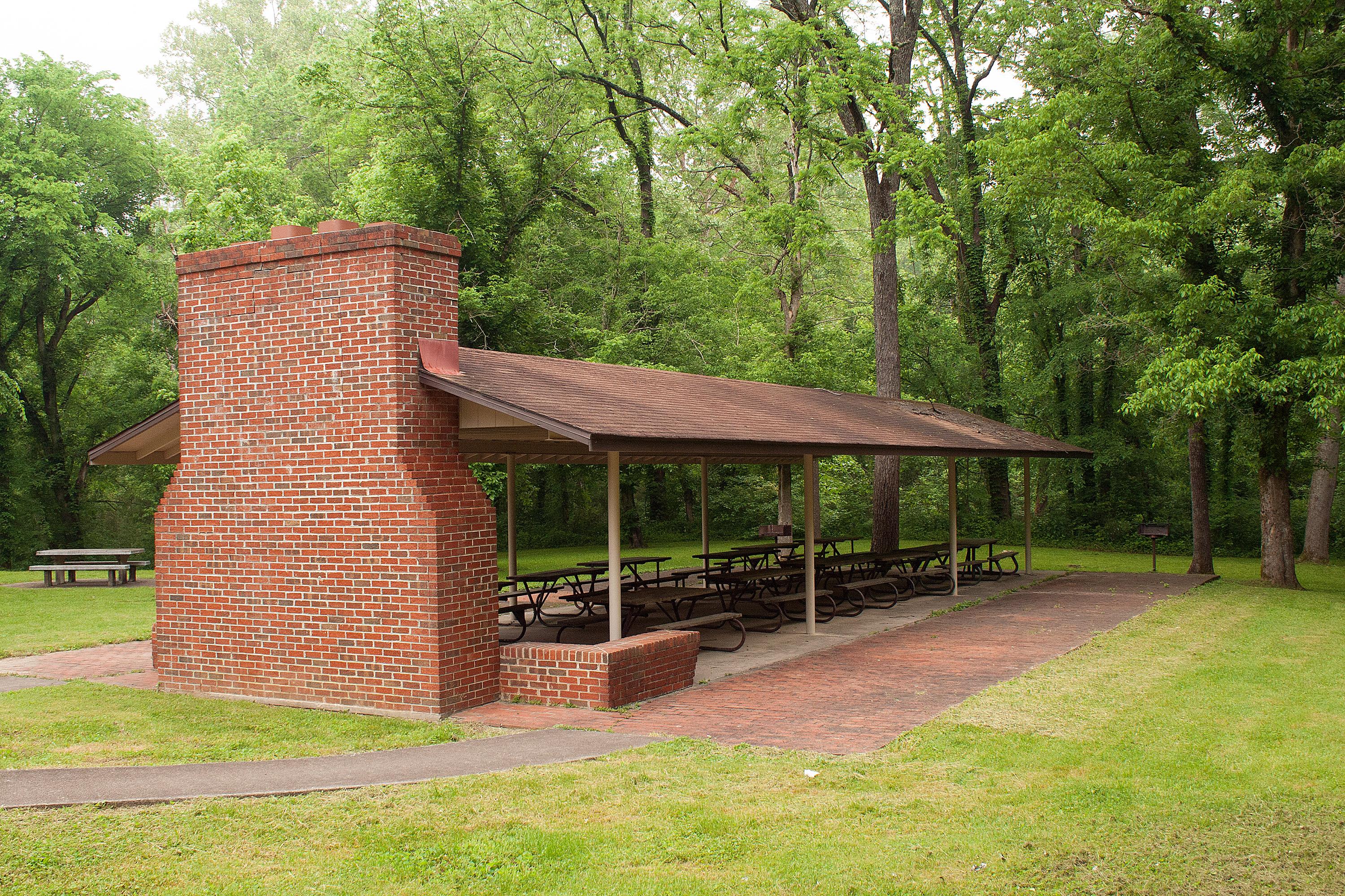 An open-air picnic shelter with multiple picnic tables and a brick fireplace.