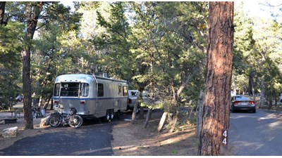 <img alt="Image: a truck with an attached trailer is parked in a paved pull-through campsite. Two bi