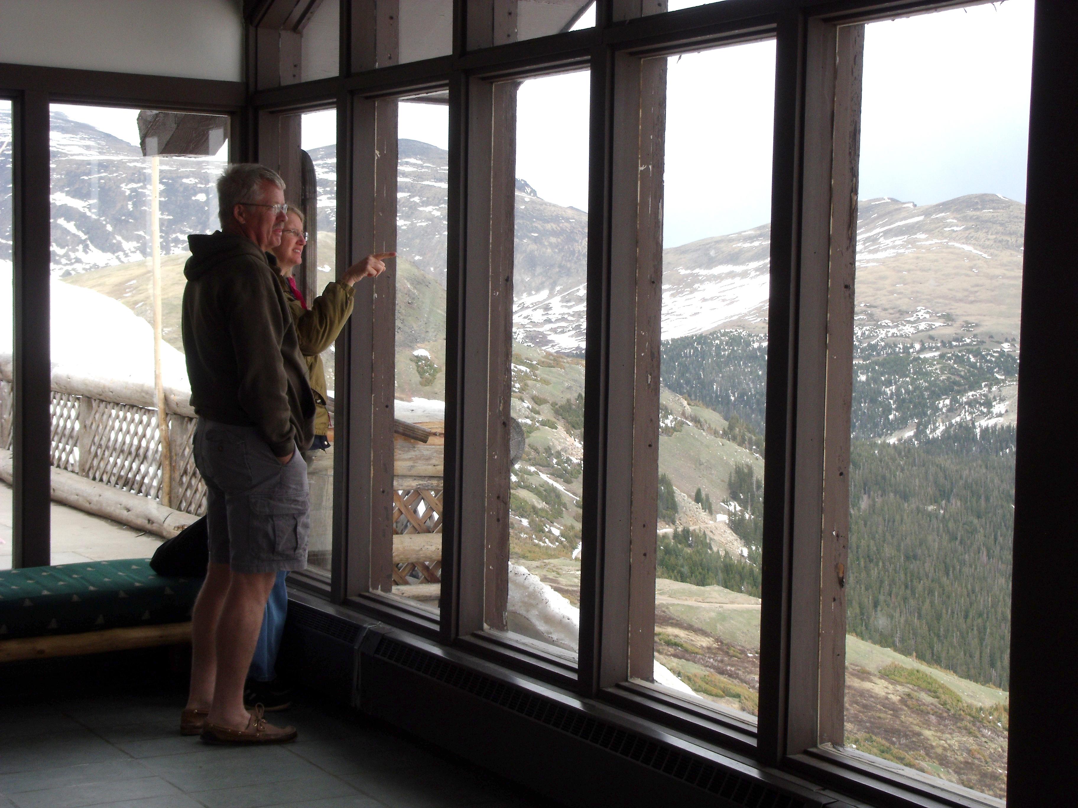 Two people are looking out at mountain peaks from the windows of Alpine Visitor Center