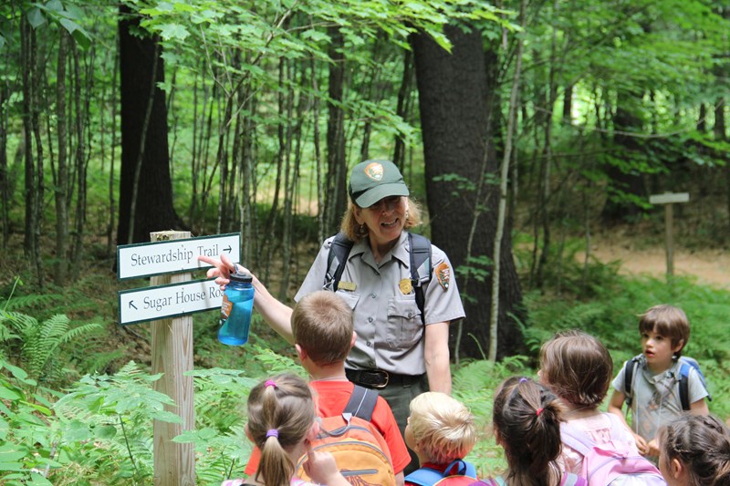 Fun in the Forest camp Park Ranger points to a trail sign and talks to a group of young children