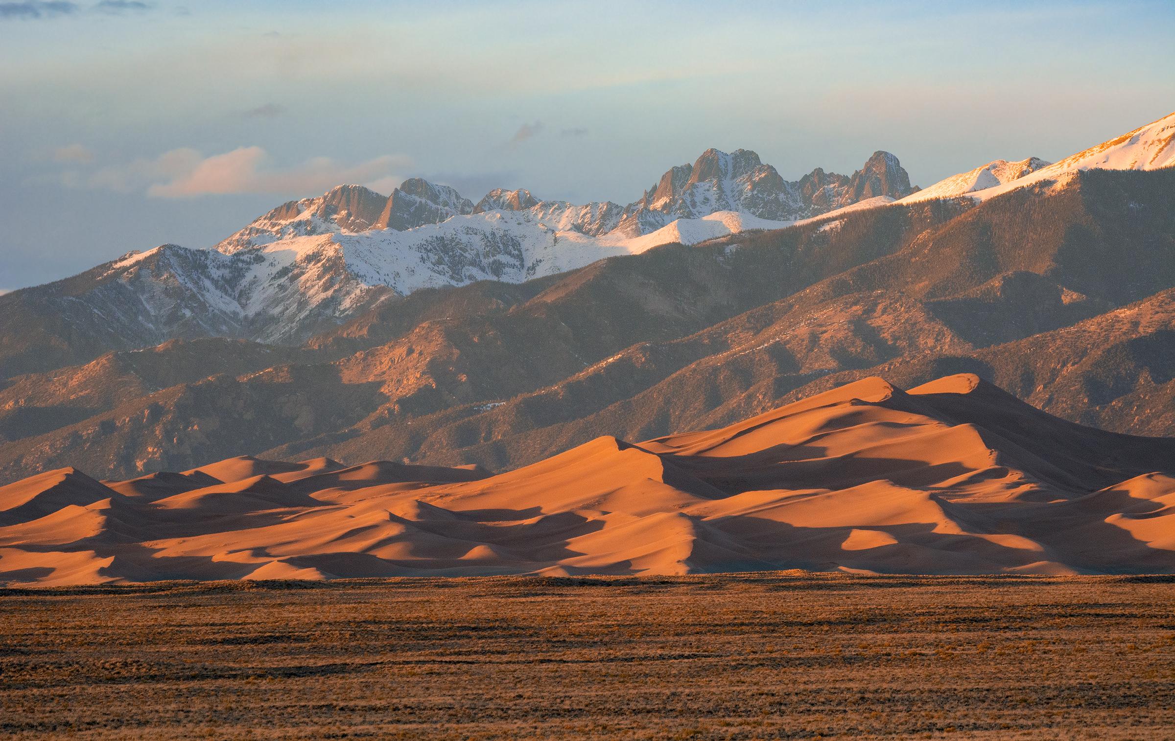 Grasslands, large dunes, and snow-capped peaks at sunset
