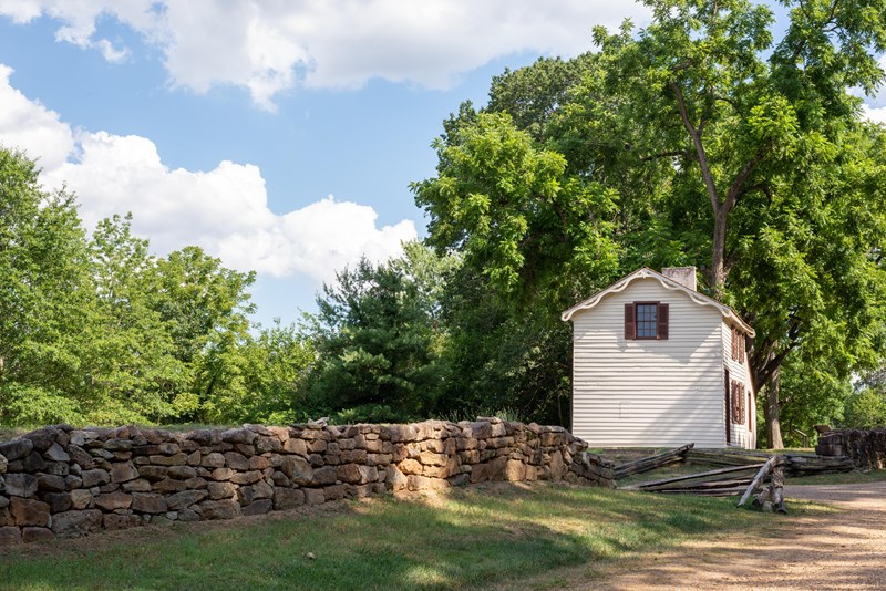 Innis House along the Sunken Road A gravel path bordered by a stone wall leading to a small, two story white house.