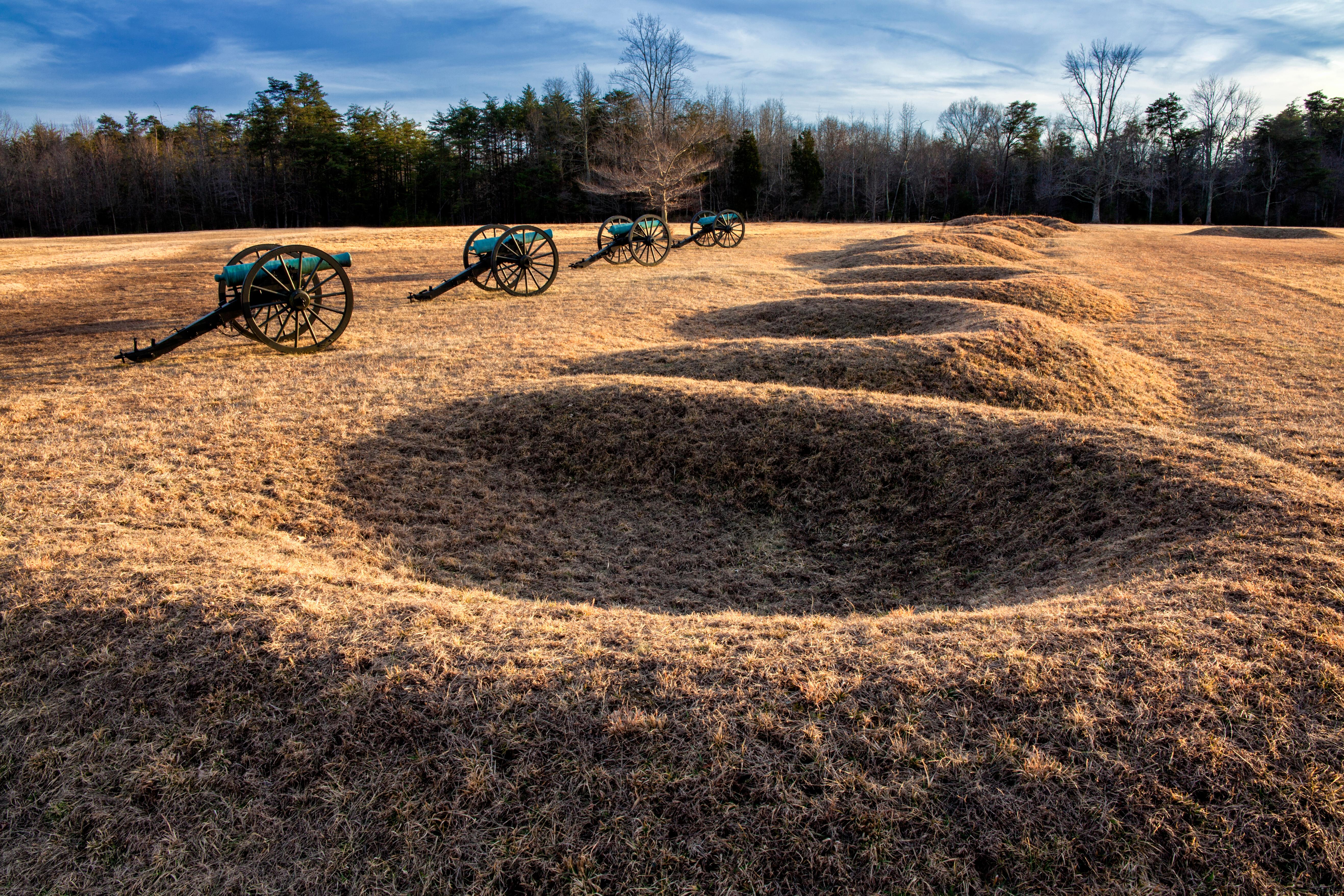 A line of four cannons placed in front of crescent shaped earthen gun pits.